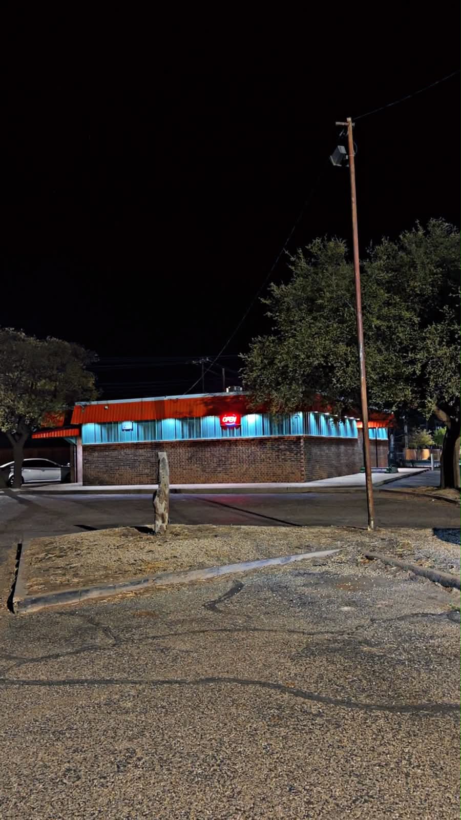 Robbins Nest at night: orange roof trim, teal panels, brick walls and a red OPEN sign