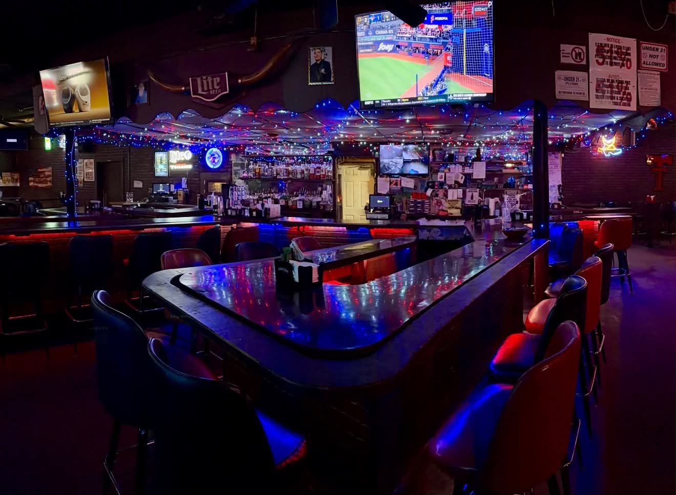 The horseshoe bar glowing red and blue under the string lights, TVs on the game