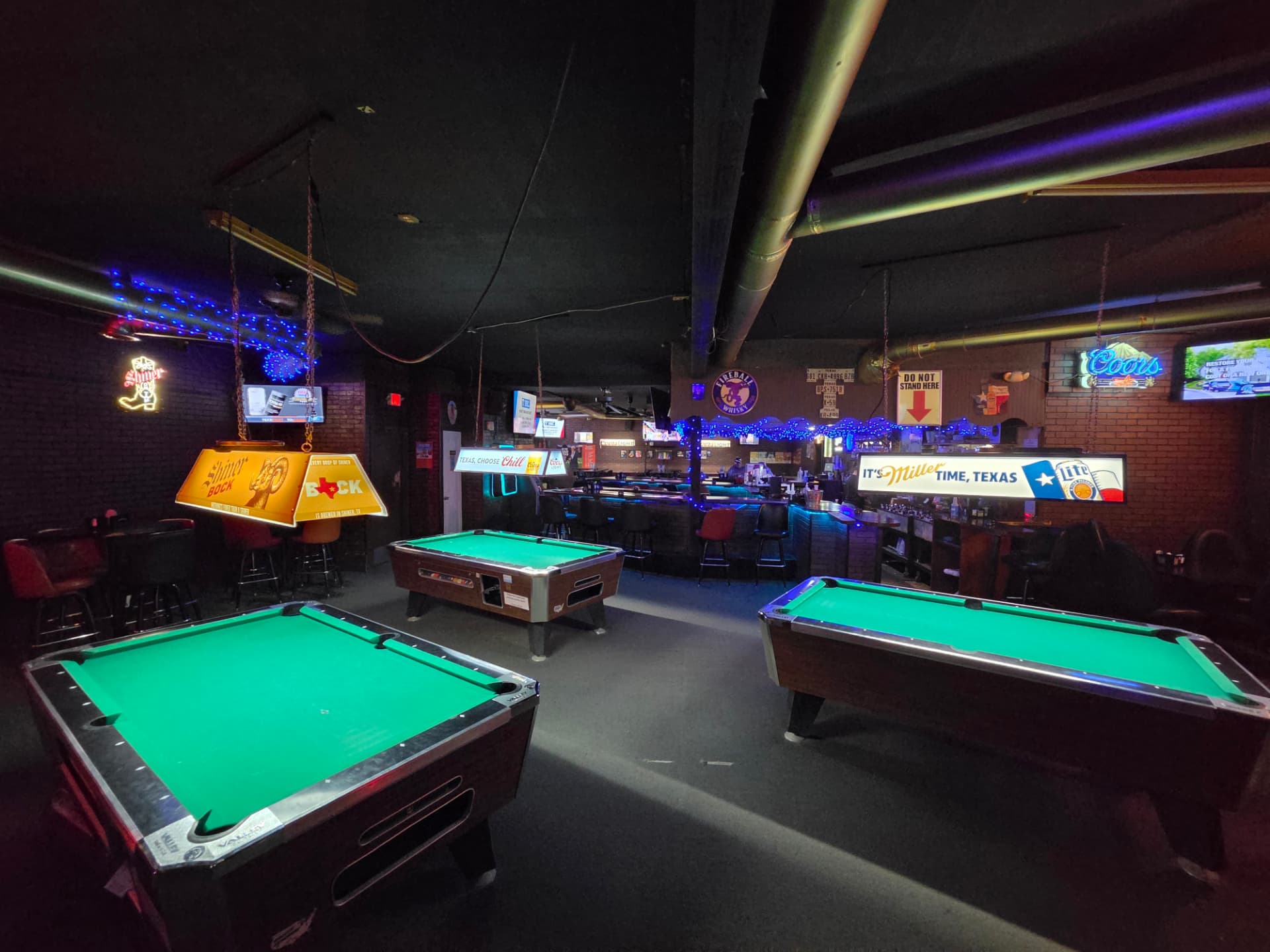 Three pool tables under Shiner Bock and Miller Lite lamps