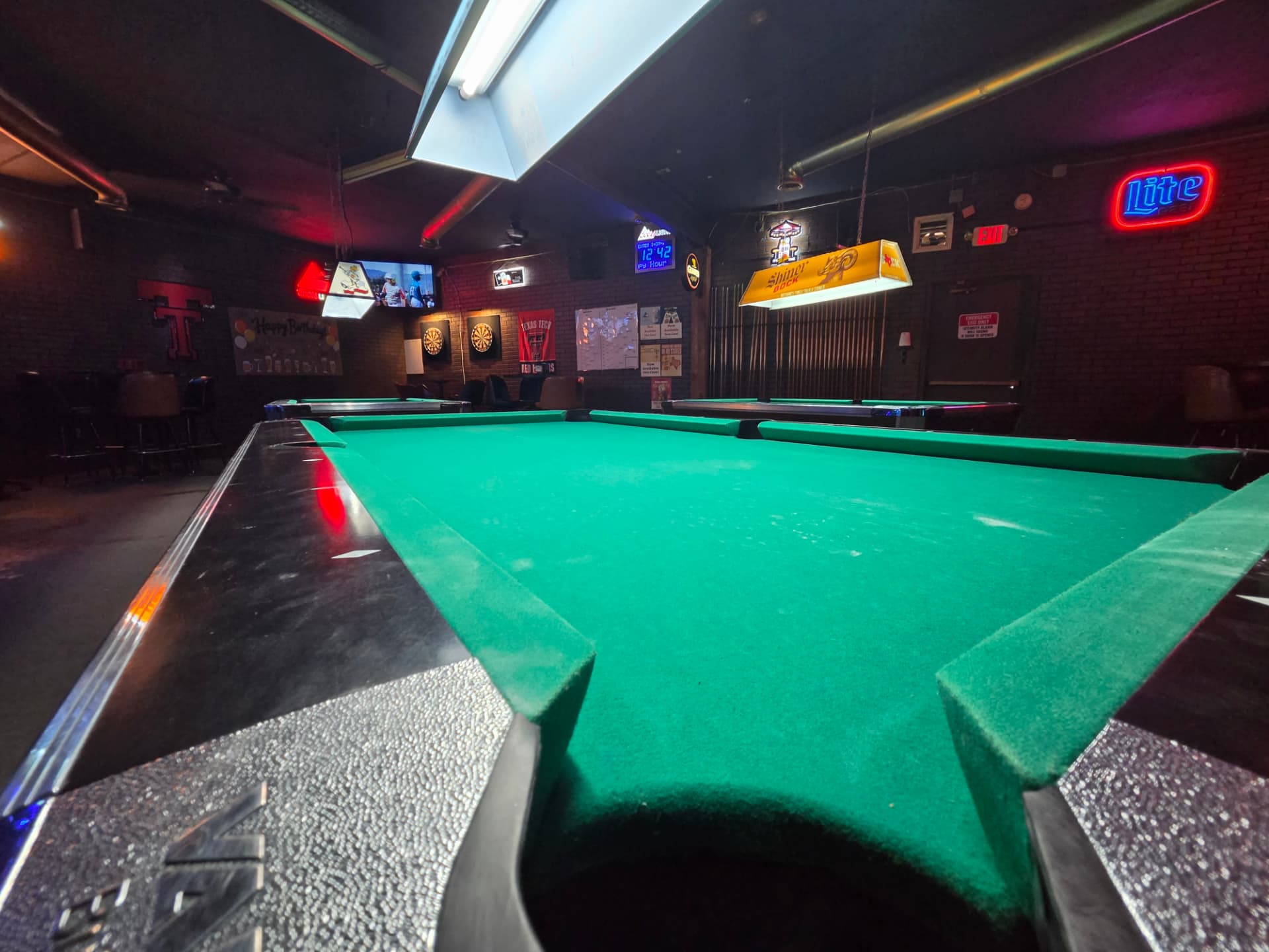 Low angle across a pool table toward the dart boards and Lite neon